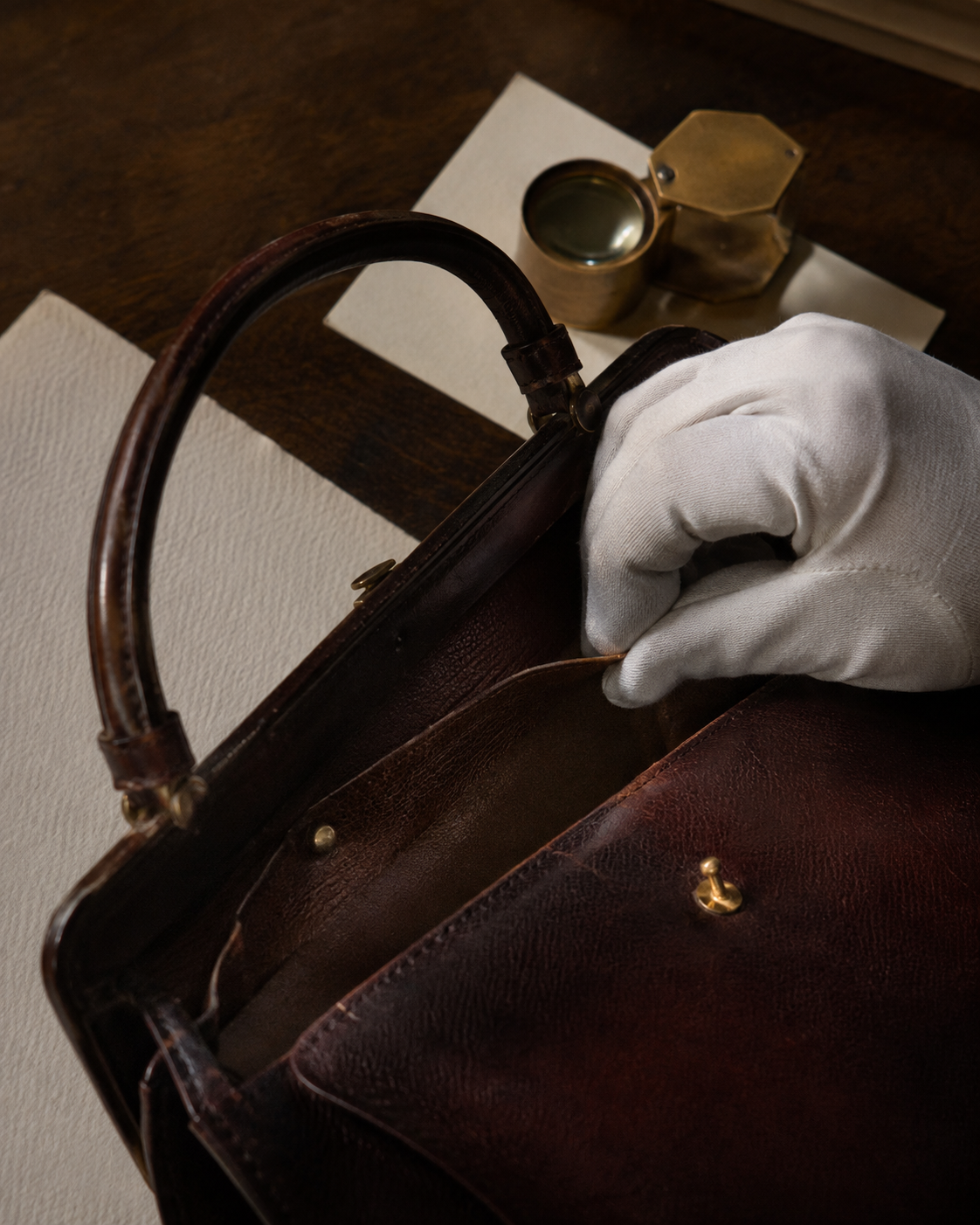 Gloved hand examining the interior construction of a vintage leather handbag