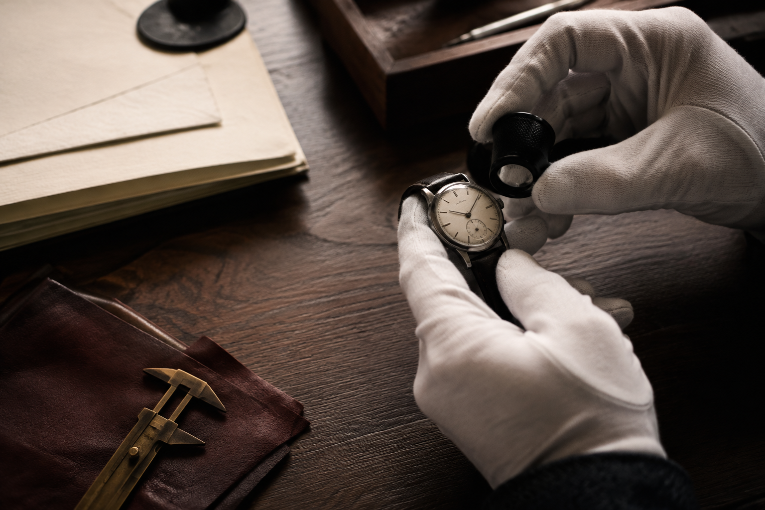 Gloved hands examining a vintage watch at an atelier workbench